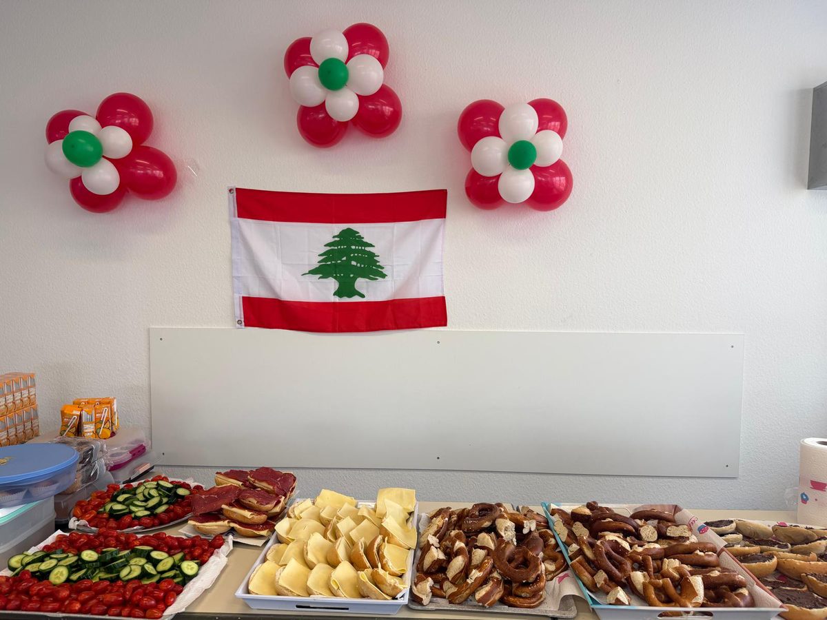 Buffet bei einem Gemeindefest: Platten mit Gemüse, Gebäck und Süßigkeiten, an der Wand die libanesische Flagge und rot-weiß-grüne Luftballons.
